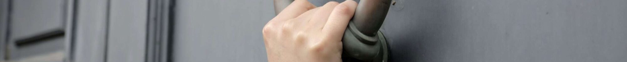 Un'inquadratura ravvicinata di una persona che bussa alla porta con un vecchio battipanni